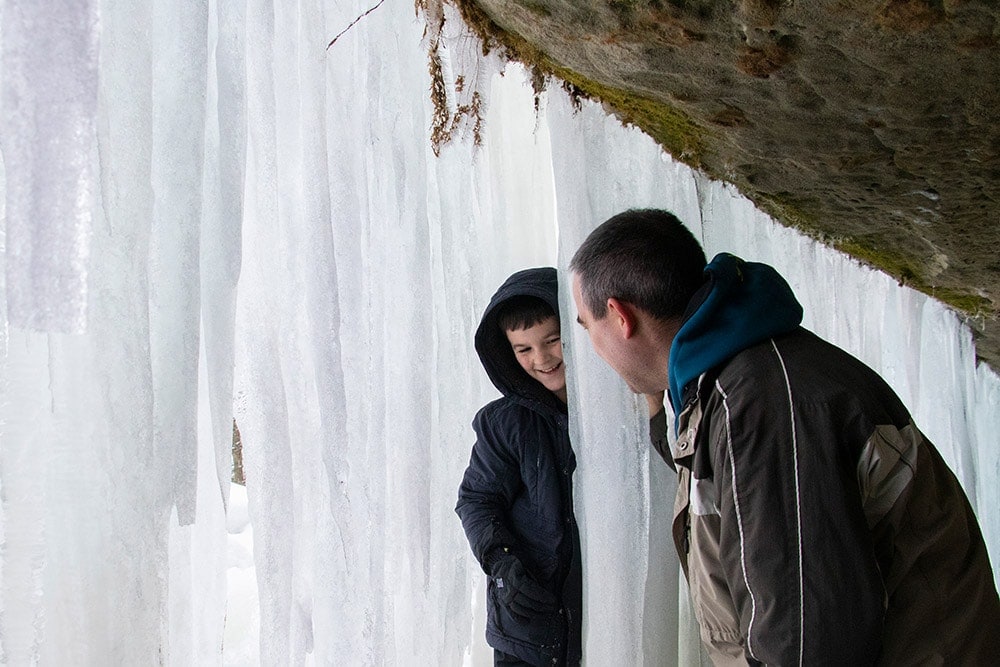 Article Title: Quotes about family trips.
Image: Father and son peeking around the large ice walls of the ice cave.