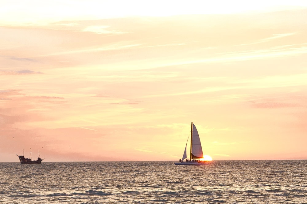 Article: Inspirational Beach Quotes
The picture is of a bright orange and yellow sunset over the ocean. There are a few sailboats sailing in the distance.