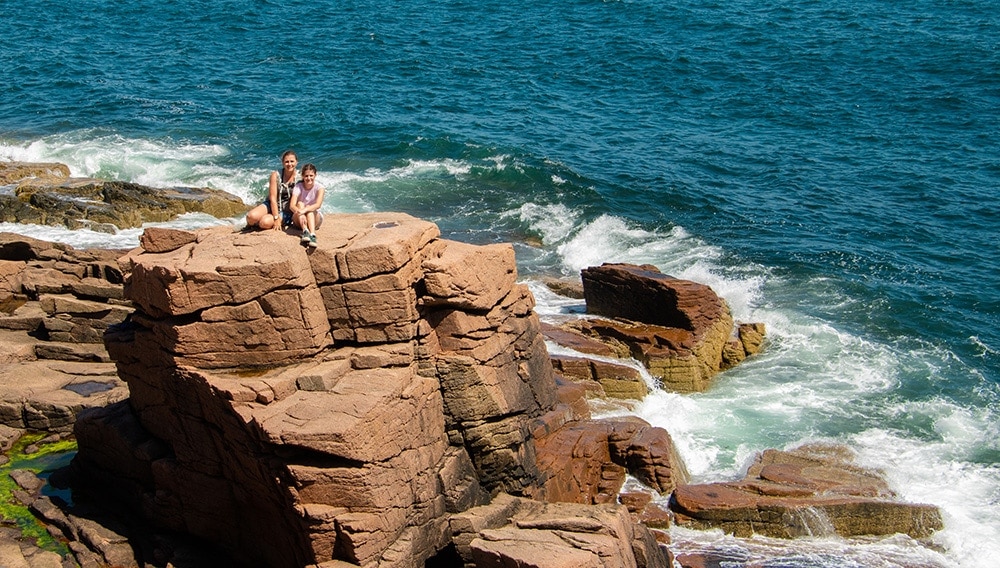 People sitting on the rocky ocean coast in Acadia National Park.