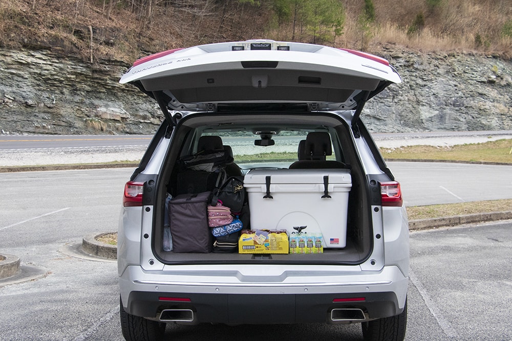 A chevy traverse with its tailgate up. You can see an orca cooler, drinks, and luggage. Food for road trips is a must on any family road trip packing list.