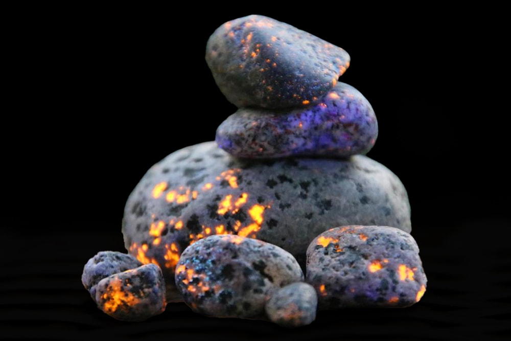 Michigan's glowing rocks (aka Yooperlites) are shown in the dark with a UV light shining on them. The rocks look like they have glowing orange specks all over them.