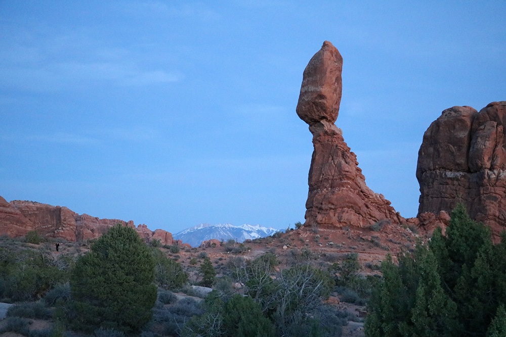 A view of Balance Rock in Arches with mountains in the background