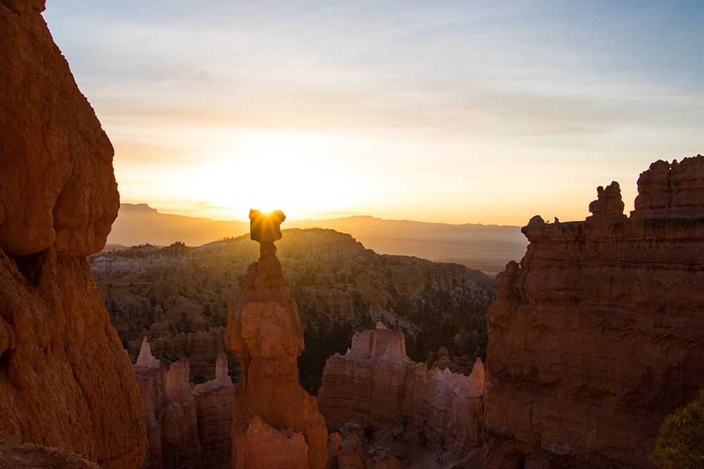 Sunrise over Thor's Hammer, a distinct rock formation in Bryce Canyon National Park. The rising sun casts a warm golden light over the iconic hoodoo, creating a breathtaking silhouette against the vibrant hues of the dawn sky, highlighting the park's natural beauty and serene ambiance.
