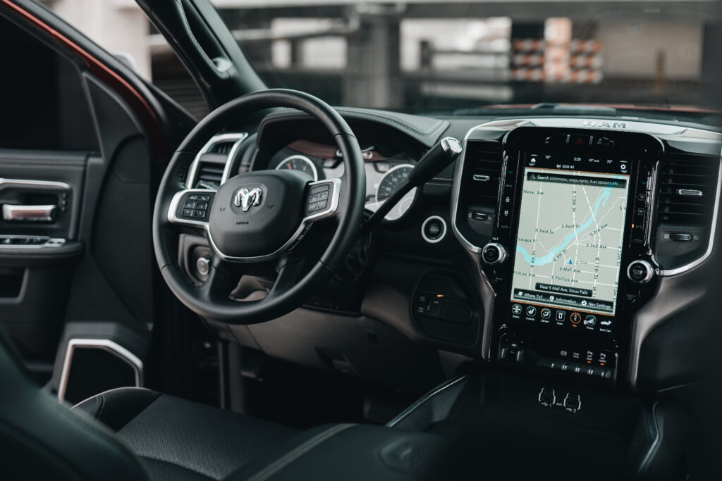 A picture of the inside of a car. The car has a black interior with black leather and a large technology display.