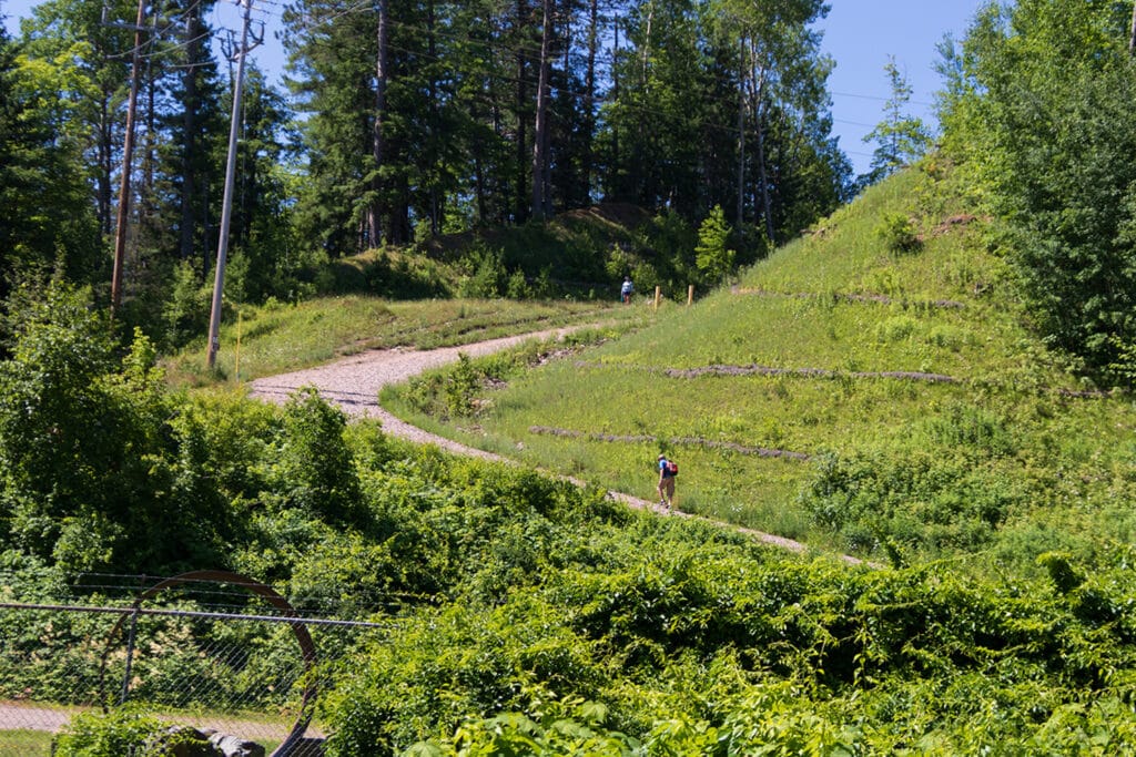 The start of Dead River Falls trail. It's a picture of a steep, gravel, access road surrounded by lush forest.