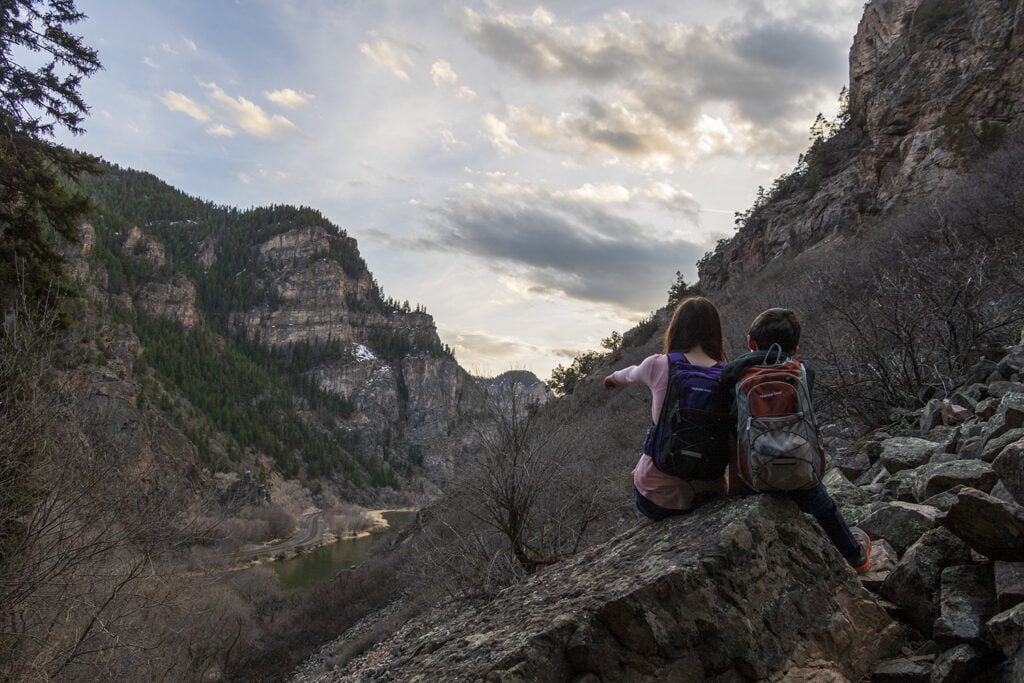 Kids sitting on a large boulder on the Hanging Lake trail overlooking the colorado river.