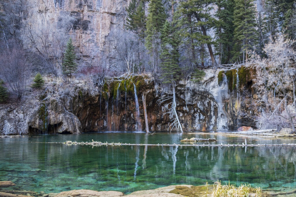 A picture of turquoise colored hanging lake and the mossy bridal veil falls flowing into the lake.
