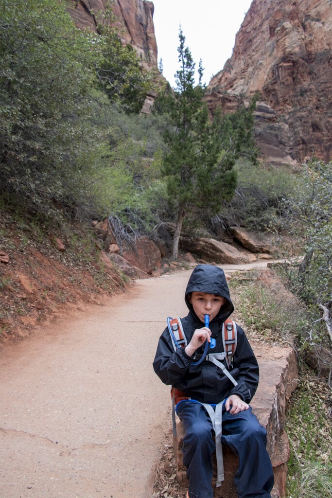 Young child staying hydrated during a hike in Zion National Park, taking a drink from his hydration backpack.