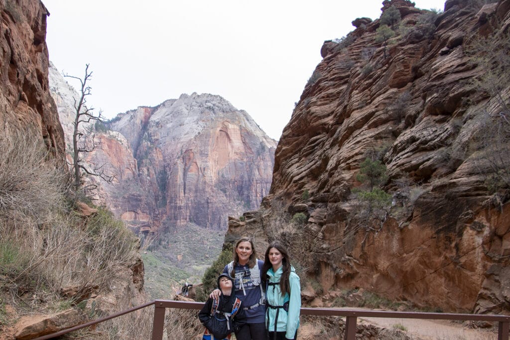 Happy family hiking in Zion National Park, framed by majestic mountains in the background. The group is surrounded by scenic beauty, capturing the essence of outdoor exploration and family adventure.