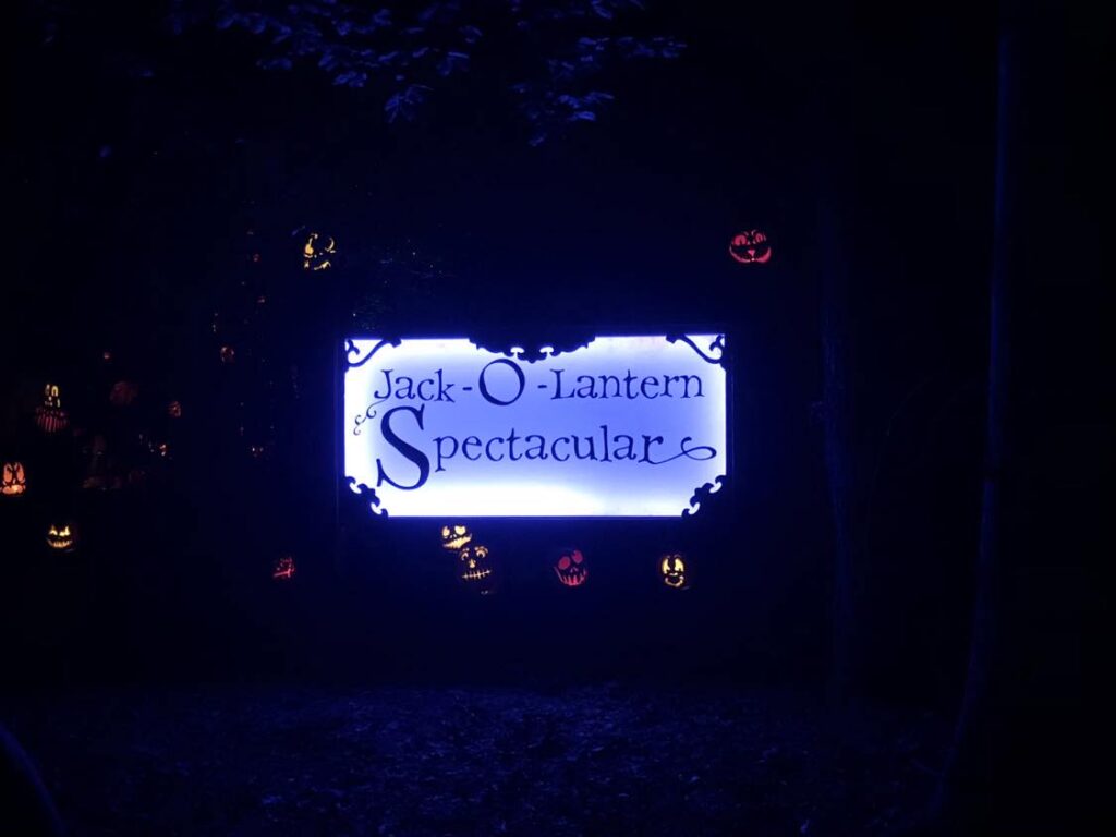 Lit up sign for the Louisville Jack O' Lantern Spectacular surrounded by Jack O' Lanterns.