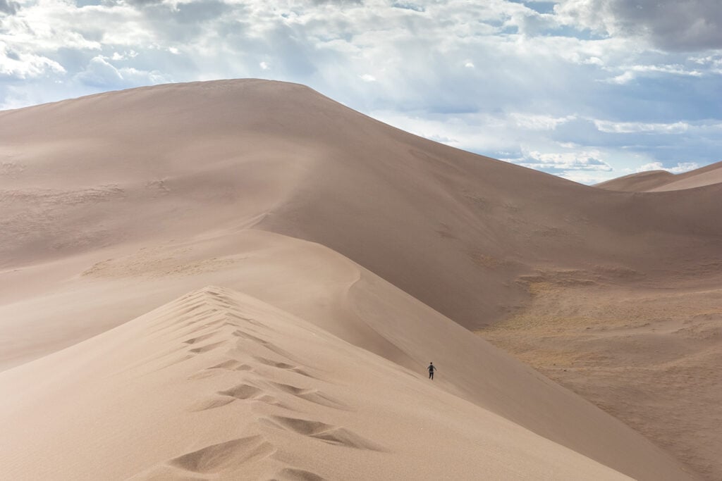 Great Sand Dunes National Park: Person walking on vast sand dunes, with blue skies in the background. A captivating desert landscape adventure.
