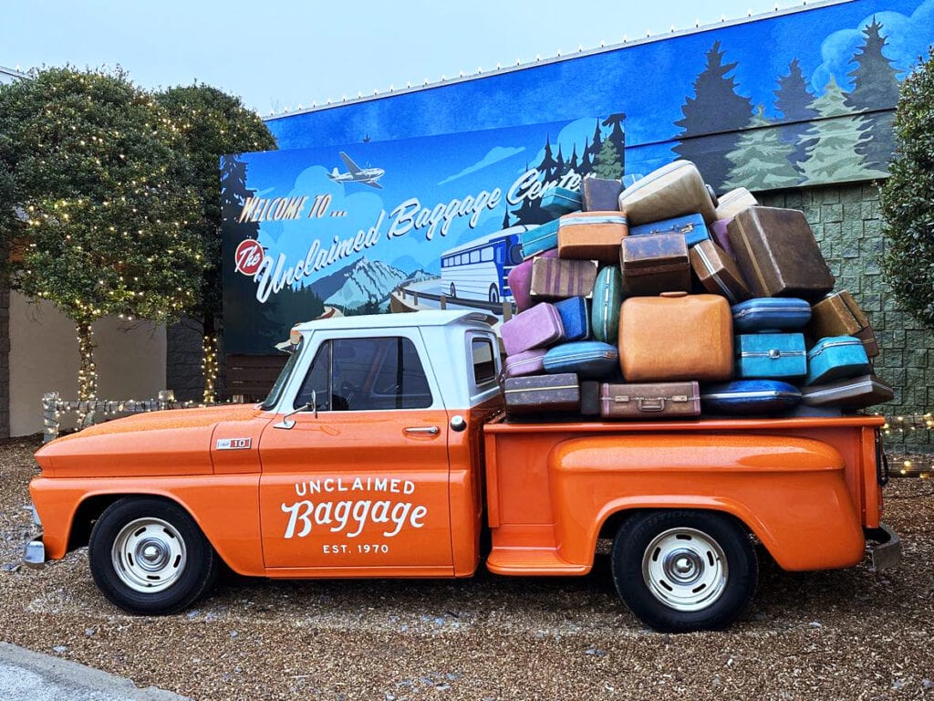 Vintage orange Unclaimed Baggage truck loaded with stacked suitcases, showcasing the unique character of this travel treasure destination.